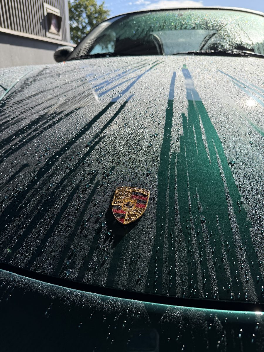 Water parelt van de keramische coating op een groene Porsche, bewijs van de waterafstotende werking